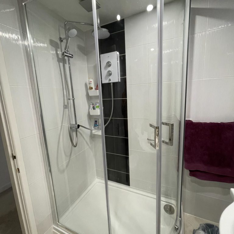 Modern shower cubicle with glass doors and wall-mounted controls. White and grey tiles.