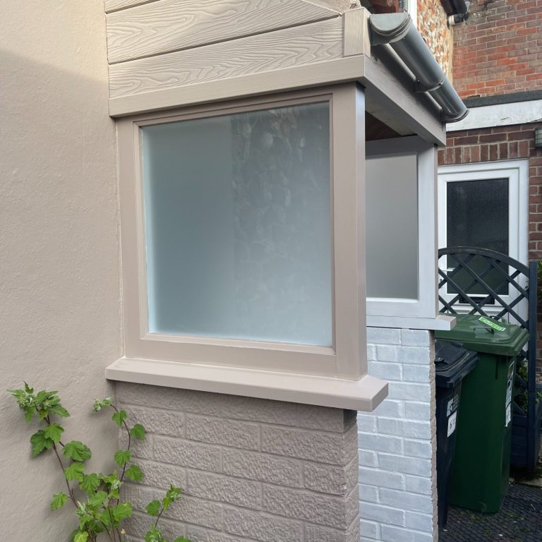 Porch featuring frosted windows with pale beige frames on top of a brick walls
