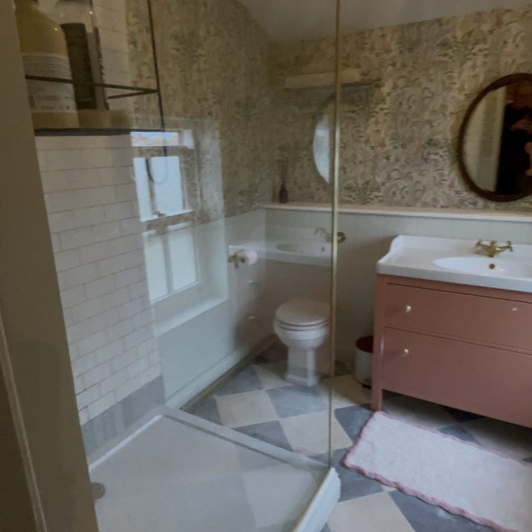 Modern bathroom featuring a shower, toilet and vanity with a round mirror, and patterned wallpaper.