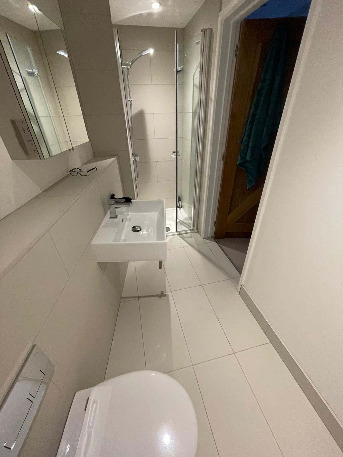 COmpleted Ensuite 1 Compact bathroom with a shower, sink, and toilet, featuring modern fixtures and tiled walls.