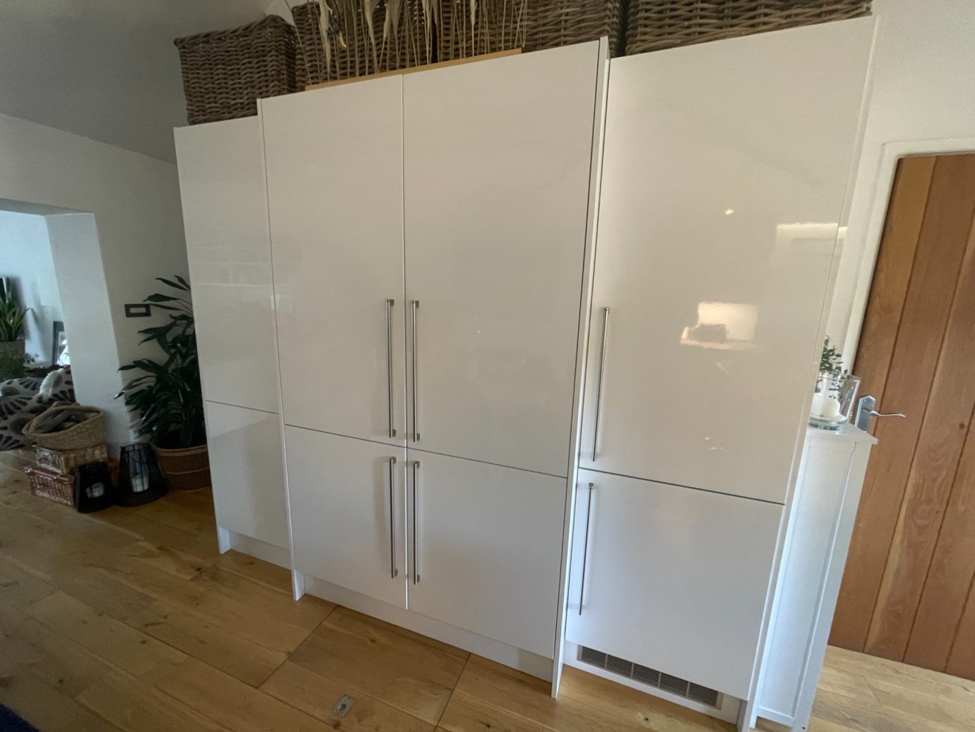 Kitchen cabinets with doors closed Modern white kitchen cabinets with sleek handles, set against a wooden floor.